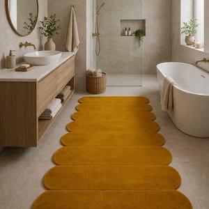 Könnte beinhalten: Senfgelber Badezimmerteppich mit einem einzigartigen, länglichen, gewellten Design. Der Teppich besteht aus einem weichen, plüschigen Material und wird vor einer Badewanne platziert. Das Badezimmer hat ein modernes Design mit neutralen Tönen und goldenen Armaturen.