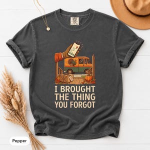May include: A charcoal grey short-sleeve t-shirt featuring a graphic of a hand holding a smartphone, a delivery van, a turkey, a package, and a pumpkin. The text reads, I BROUGHT THE THING YOU FORGOT. The shirt has a crew neckline and a relaxed fit.
