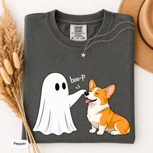 May include: A charcoal gray crewneck t-shirt featuring a graphic of a white ghost touching the nose of a brown and white Corgi dog. The text "boo-p" is printed above the dog. The shirt has a Comfort Colors label inside the collar.