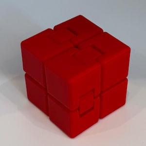 May include: A bright red puzzle cube with a unique interlocking design. The cube is composed of several smaller, rectangular blocks that fit together to form the larger cube shape. The vibrant red color and geometric form make it visually striking.