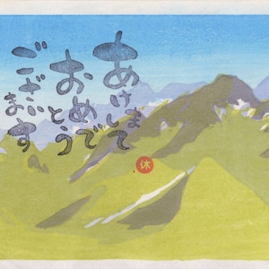 May include: A woodblock print depicting a mountain range with a blue sky and white clouds. The mountains are green and brown with snow-capped peaks. The print is signed in Japanese characters.