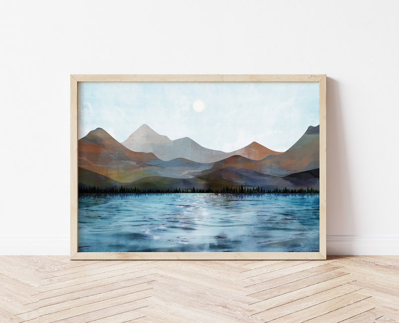 Puede incluir: Una impresi&oacute;n art&iacute;stica enmarcada que representa un sereno paisaje lacustre con monta&ntilde;as al fondo. La obra de arte muestra un lago azul que refleja el cielo y un sol brillante. Las monta&ntilde;as est&aacute;n representadas en tonos marrones, azules y verdes.