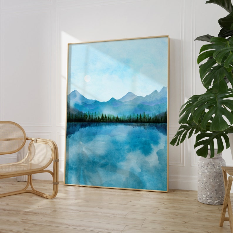 May include: A watercolor painting of a mountain range reflected in a still lake. The mountains are painted in shades of blue and green, with a light blue sky above. The lake is a deep blue, with white clouds reflected in the water.
