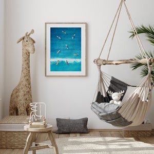 May include: A framed photograph of a blue ocean with several surfboards floating on the surface. The photo is hanging on a white wall in a room with a hanging hammock and a giraffe-shaped statue.