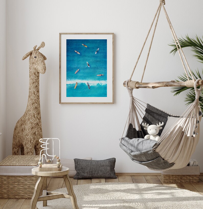 May include: A framed photograph of a blue ocean with several surfboards floating on the surface. The photo is hanging on a white wall in a room with a hanging hammock and a giraffe-shaped statue.