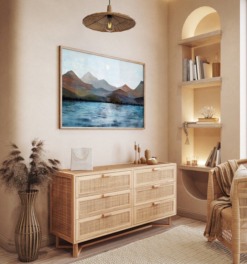 Puede incluir: Una escena interior serena con una pintura enmarcada de monta&ntilde;as y agua. Debajo de la obra de arte hay una c&oacute;moda de madera clara con cajones de rat&aacute;n tejido. Una l&aacute;mpara colgante tejida cuelga arriba y una silla tejida est&aacute; en la esquina. La habitaci&oacute;n tiene una paleta de colores neutros.