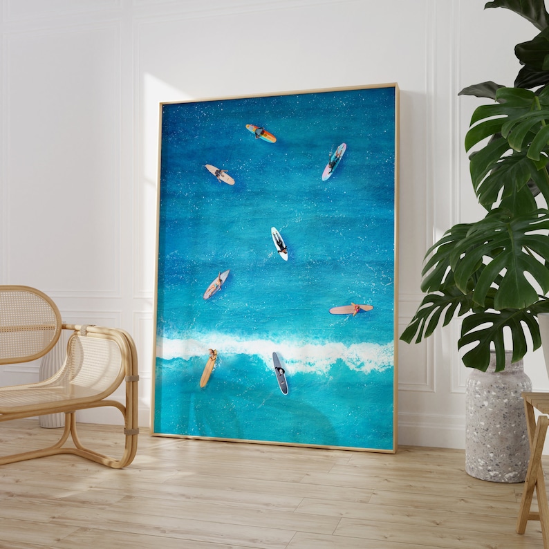 May include: A blue and white abstract painting of surfers on turquoise water with white foamy waves. The painting is framed in a thin gold frame.