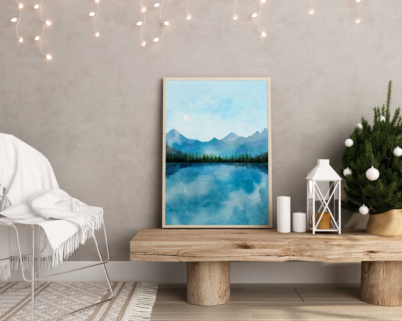 May include: A framed watercolor painting of a mountain lake scene with a blue sky and white clouds. The lake is reflecting the mountains and sky. The painting is on a wooden shelf with a white lantern and candles.