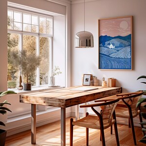 Puede incluir: Un escritorio de madera con un acabado de madera clara y dos sillas. El escritorio tiene una ventana grande detr&aacute;s y una impresi&oacute;n enmarcada de un paisaje azul con una casa blanca. La impresi&oacute;n tiene el texto "The Hills Are Alive".