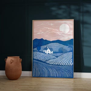Puede incluir: Una impresi&oacute;n enmarcada de un paisaje azul y blanco con una peque&ntilde;a casa blanca y una gran luna blanca en el cielo. El cielo es de color rosa claro.