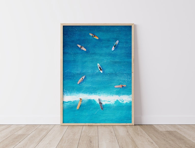 May include: An aerial view of a group of people on surfboards in a blue ocean with white waves. The surfboards are various colors and sizes.