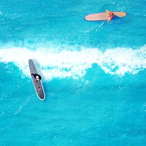 May include: Two people are surfing on blue water. One person is on a black surfboard and the other is on a brown surfboard.