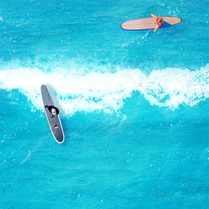 May include: Two people are surfing on blue water. One person is on a black surfboard and the other is on a brown surfboard.