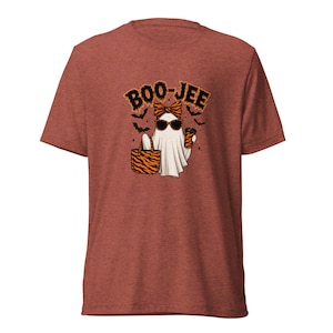 May include: A heathered rust-coloured short-sleeve t-shirt featuring a graphic of a ghost wearing a tiger-print bow and sunglasses, holding a matching tote bag and a coffee cup, with the text BOO-JEE and small black bats printed above.