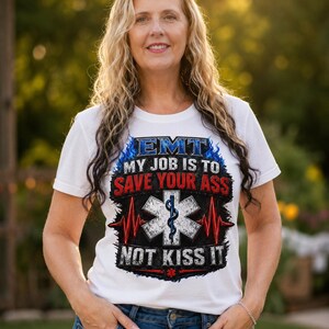 May include: A white short-sleeved t-shirt featuring a graphic print with the text EMT MY JOB IS TO SAVE YOUR ASS NOT KISS IT, accompanied by a Star of Life symbol, a blue flame design, and a red EKG heart rhythm line across the chest.