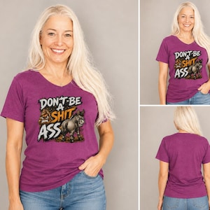 May include: A heathered purple V-neck t-shirt featuring a graphic print on the front. The design includes a cartoon poop emoji and a donkey illustration with the text "DON'T BE A SHIT ASS" in bold, stylised white and orange lettering.