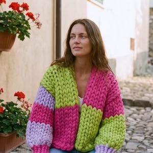 May include: A chunky knit cardigan in a color block design. The sweater features sections of lime green, lavender, and hot pink. The open front cardigan is made of thick yarn and has long sleeves.