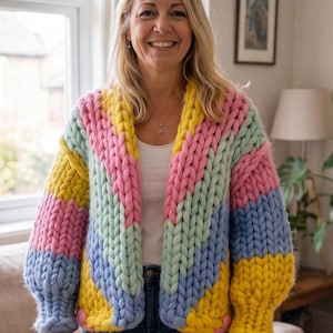 May include: A chunky knit cardigan featuring a vibrant chevron pattern in pastel pink, light blue, mint green, and bright yellow. This open-front sweater is crafted from thick, oversized yarn with long sleeves and ribbed cuffs, creating a textured look.