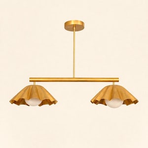 Puede incluir: Lámpara colgante dorada de dos luces. La lámpara tiene una barra horizontal con dos pantallas festoneadas, cada una con una bombilla blanca. Se suspende del techo mediante una varilla vertical.