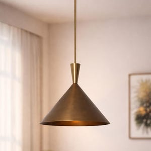 Puede incluir: Lámpara colgante de latón con pantalla cónica. La luz cuelga de una varilla de latón y un soporte de techo circular. La pantalla tiene un acabado metálico cálido. La lámpara está suspendida en una habitación con tonos neutros.