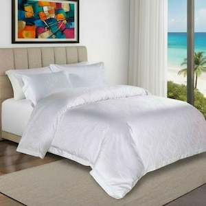 May include: A white bed set with a subtle patterned design. The bed includes a duvet cover, pillows, and sheets. The bedroom has a neutral colour scheme. A colourful painting hangs on the wall above the bed.
