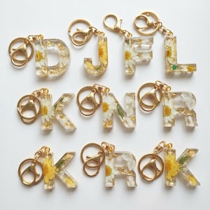 Pode incluir: Uma caneca de cerâmica branca com uma alça preta e o texto "But First, Coffee" em preto, com uma fonte manuscrita. A caneca está sobre uma superfície branca.