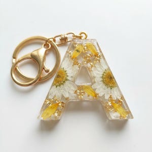 Pode incluir: Uma caneca de cerâmica branca com uma alça preta e o texto "But First, Coffee" em preto, com uma fonte manuscrita. A caneca está sobre uma superfície branca.