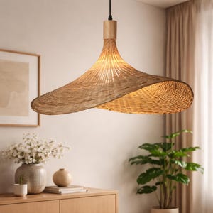 Peut inclure: Suspension luminaire en rotin tressé avec un abat-jour large en forme de chapeau. La lampe est de couleur marron clair naturel et est suspendue à une base en bois et un cordon noir. Le luminaire est conçu pour l'intérieur.