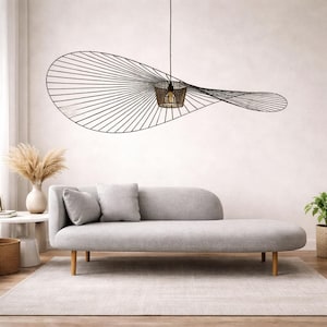 Può includere: Un moderno soggiorno con una chaise longue grigia e due cuscini abbinati, una grande lampada a sospensione con struttura in filo nero e un tappeto dai toni neutri. Un vaso di erba della pampa essiccata e una pianta in vaso completano l'arredamento.