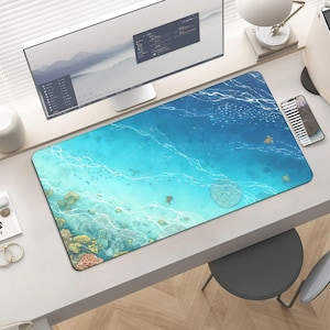 May include: A rectangular desk mat featuring an ocean scene with coral reefs, turtles, and fish. The mat's design showcases varying shades of blue and turquoise, creating a vibrant underwater aesthetic. The mat is placed on a white desk, with a computer monitor in the background.