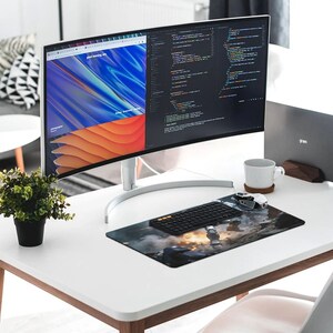 Puede incluir: Un espacio de trabajo moderno con un monitor de computadora curvo que muestra c&oacute;digo y un sitio web. Un teclado negro, un rat&oacute;n y una alfombrilla de rat&oacute;n con gr&aacute;ficos est&aacute;n sobre el escritorio blanco. Tambi&eacute;n hay una peque&ntilde;a planta en maceta y una taza blanca.
