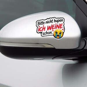 Könnte beinhalten: Ein weißer Vinyl-Aufkleber auf einem silbernen Auto-Außenspiegel. Der Aufkleber zeigt den schwarzen Text 'Bitte nicht hupen' über dem roten Text 'ich WEINE' und 'schon.' sowie ein weinendes gelbes Emoji-Gesicht mit blauen Tränen.