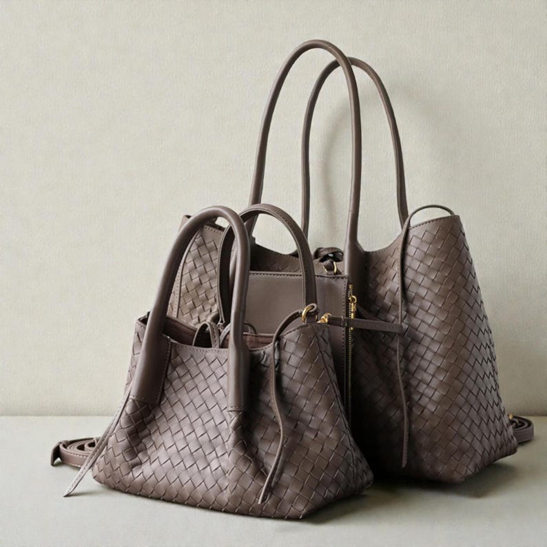May include: Two brown woven leather handbags with top handles and a shoulder strap. The bags are different sizes, with the smaller one in the foreground and the larger one behind it. The bags have a classic, elegant design.