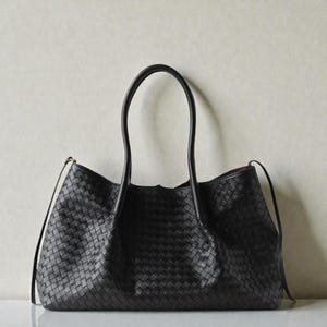 May include: A black tote bag with a woven pattern. The bag features two long, curved handles and a rectangular form. The bag is made of a dark material and has a simple, elegant design.
