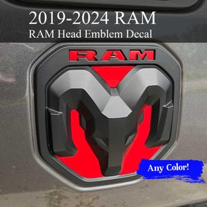 May include: A black and red RAM Head emblem decal for 2019-2024 RAM trucks. The decal features the RAM logo in red, with the text "RAM" in red. The decal is shown on a gray vehicle surface. The text "Any Color!" is in a blue rectangle.