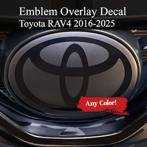 以下が含まれることがあります： 2016年から2025年までのトヨタRAV4モデル用エンブレムオーバーレイデカール。画像は、濃いグレーのトヨタのロゴが入った車のフロントグリルをクローズアップで表示しています。「Any Color!」というテキストが赤いバナーで表示されています。