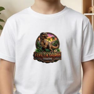 May include: A white short-sleeved t-shirt featuring a circular graphic of a brown Tyrannosaurus Rex standing in a tropical landscape with palm trees at sunset. Below the dinosaur, a stone-textured plaque displays the text FIVE-A-SAURUS MARK.