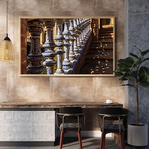 Könnte beinhalten: Gerahmtes Foto einer detaillierten architektonischen Szene. Das Bild zeigt eine Reihe verzierter Säulen mit blau-weißen Keramikfliesenmustern, die zu einer Treppe führen. Das Foto wird über einem Holztisch mit zwei Stühlen angezeigt.