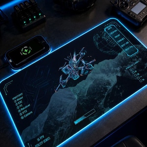 May include: A rectangular desk mat with a black surface and a glowing blue LED border. The mat features a graphic of an FPV drone, a globe, and technical text including "Anatomy," "S6 FPV Utility Series," and a checklist for flight data.