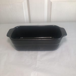 May include: A rectangular black baking dish with a smooth, glossy finish and integrated handles on both ends. The vessel features deep, straight sides and a flat base, designed for oven use. The dark, uniform color covers the entire exterior.