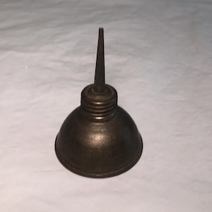 May include: A vintage-style metal oil can featuring a rounded, dome-shaped base and a narrow, tapered spout. The object has a dark, weathered bronze-toned finish with visible horizontal threading around the neck where the spout connects to the body.
