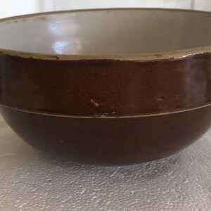 May include: A brown ceramic bowl with a light interior. The bowl has a wide, rounded rim and a slightly flared shape. The exterior is a rich, dark brown color, while the interior is a lighter, off-white hue. This bowl is suitable for kitchen use.
