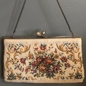 Puede incluir: Bolso de mano de cuentas color marfil con un diseño de tapiz floral. El bolso rectangular presenta un marco plateado y un asa de cadena. El tapiz incluye flores rojas, amarillas, azules y verdes con detalles dorados.