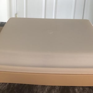 May include: A beige rectangular food storage container with a matching lid. The container is sitting on a dark surface. The lid is slightly lighter in color than the base.