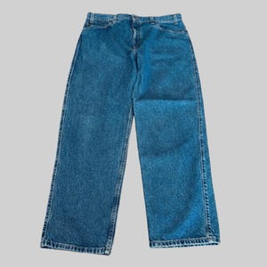 May include: A pair of blue denim jeans with a classic five-pocket design. The jeans have a straight leg cut and a medium wash. The stitching is a contrasting gold color. The jeans are laid flat on a light gray background.