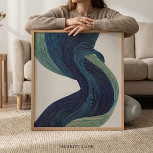 Op de afbeelding: Abstracte kunstprint met vloeiende lijnen in blauw- en groentinten. Het kunstwerk is ingelijst in een natuurlijke houten lijst. De tekst "MERRITT LANE" staat onderaan afgedrukt.