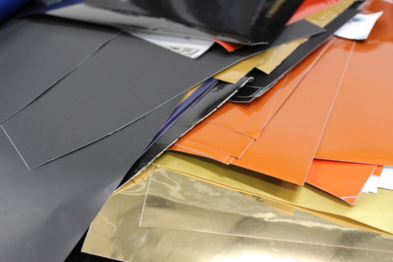 May include: A stack of various coloured vinyl sheets, including black, orange, gold, and grey. The sheets are arranged in a random order, with some overlapping.