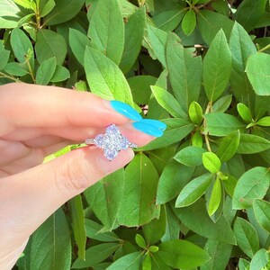 以下が含まれることがあります： 四つ葉のクローバーの形に配置された4つの丸い透明なファセットカットストーンの中央クラスターを特徴とするシルバー調のリング。バンドは細い金属製で、見える部分のシャンクに沿って小さな透明な輝くストーンがアクセントになっています。