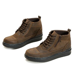 Peut inclure: Paire de bottines en cuir marron avec semelles noires. Les bottines présentent un laçage, une fermeture éclair latérale et des coutures décoratives. Aspect robuste et texturé, adapté au port décontracté. Sur fond blanc.