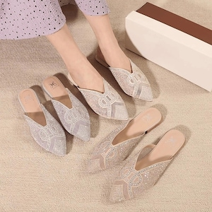 May include: A collection of elegant, light-colored mule-style shoes with pointed toes. The shoes feature intricate embellishments, including sparkling rhinestones and delicate mesh detailing. The design is feminine and suitable for special occasions.